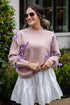 Woman wearing a pink sweater with purple accents and a white skirt outdoors.