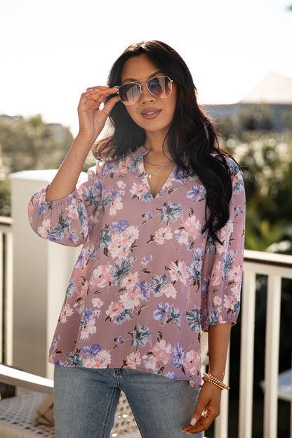 Woman wearing a floral blouse and sunglasses on a balcony with palm trees in the background