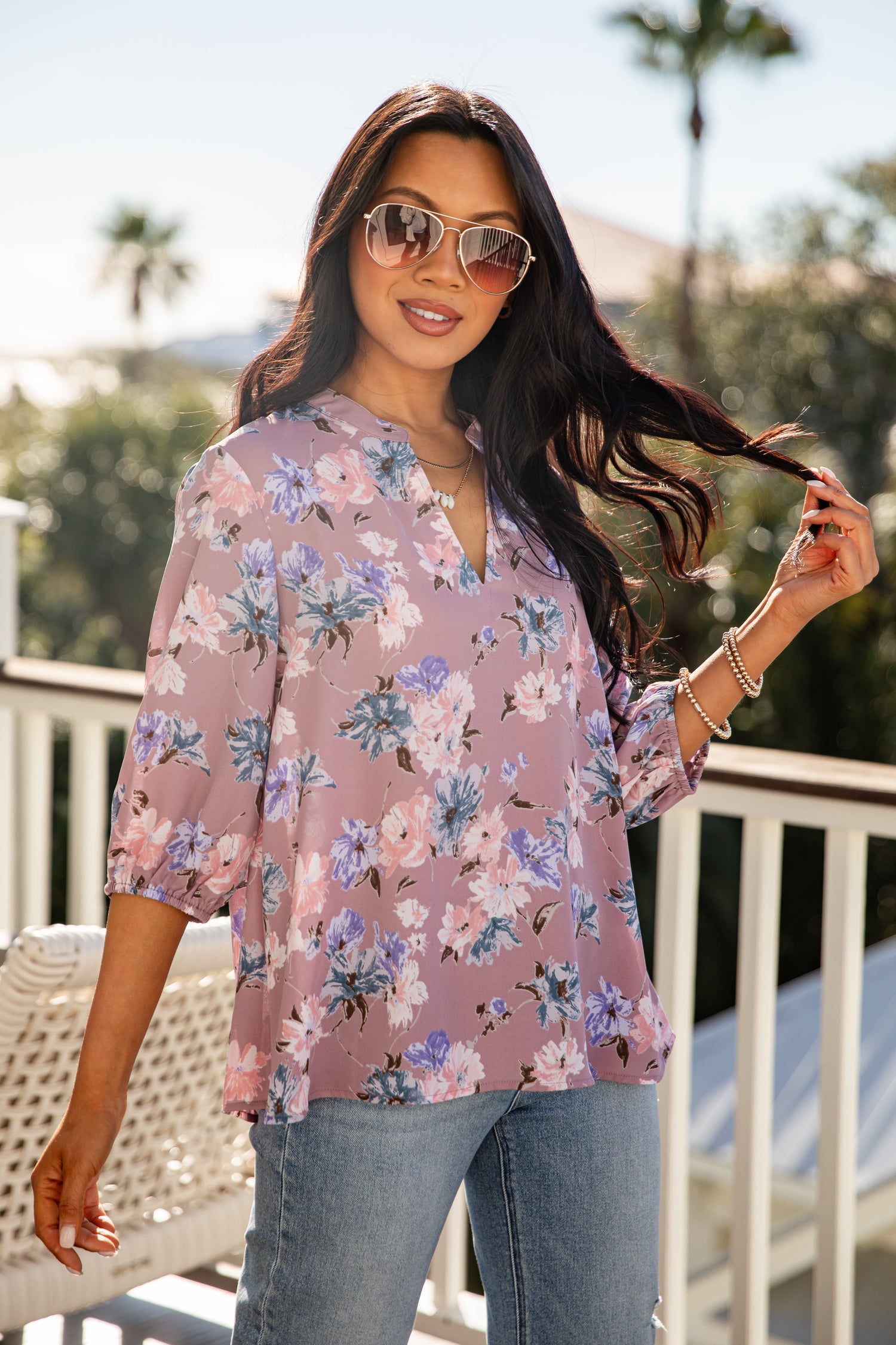 Woman wearing a floral blouse and sunglasses on a balcony with palm trees in the background