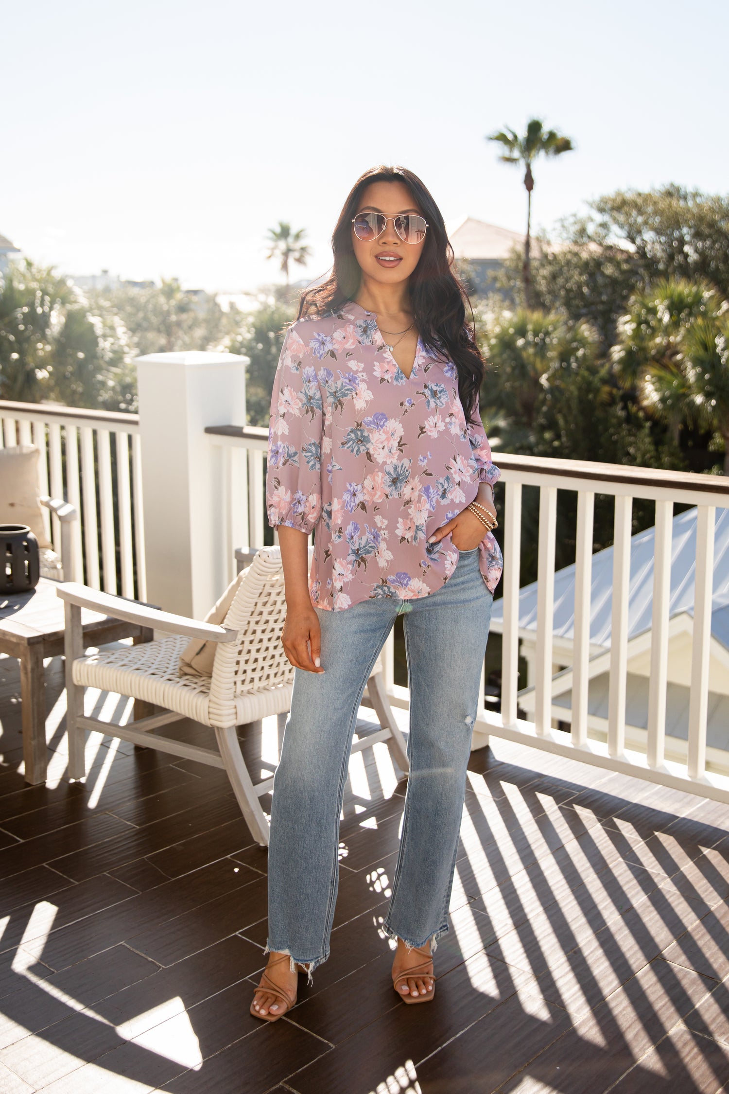 Woman wearing a floral blouse and sunglasses on a balcony with palm trees in the background