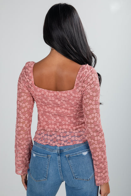 Person wearing a pink floral long-sleeve top and blue jeans on a plain background