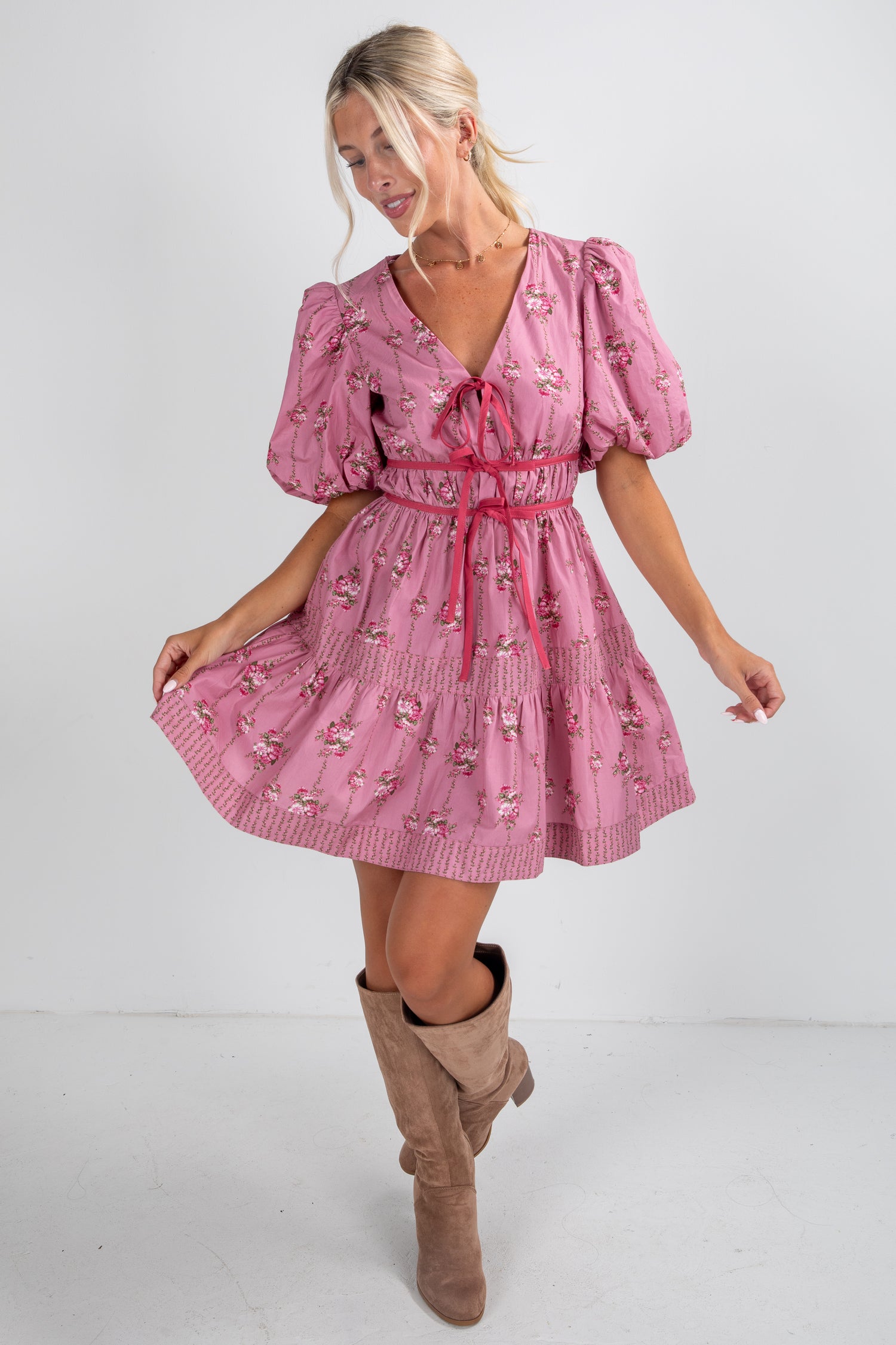 Woman wearing a pink dress with puff sleeves and a red belt, standing against a white background.