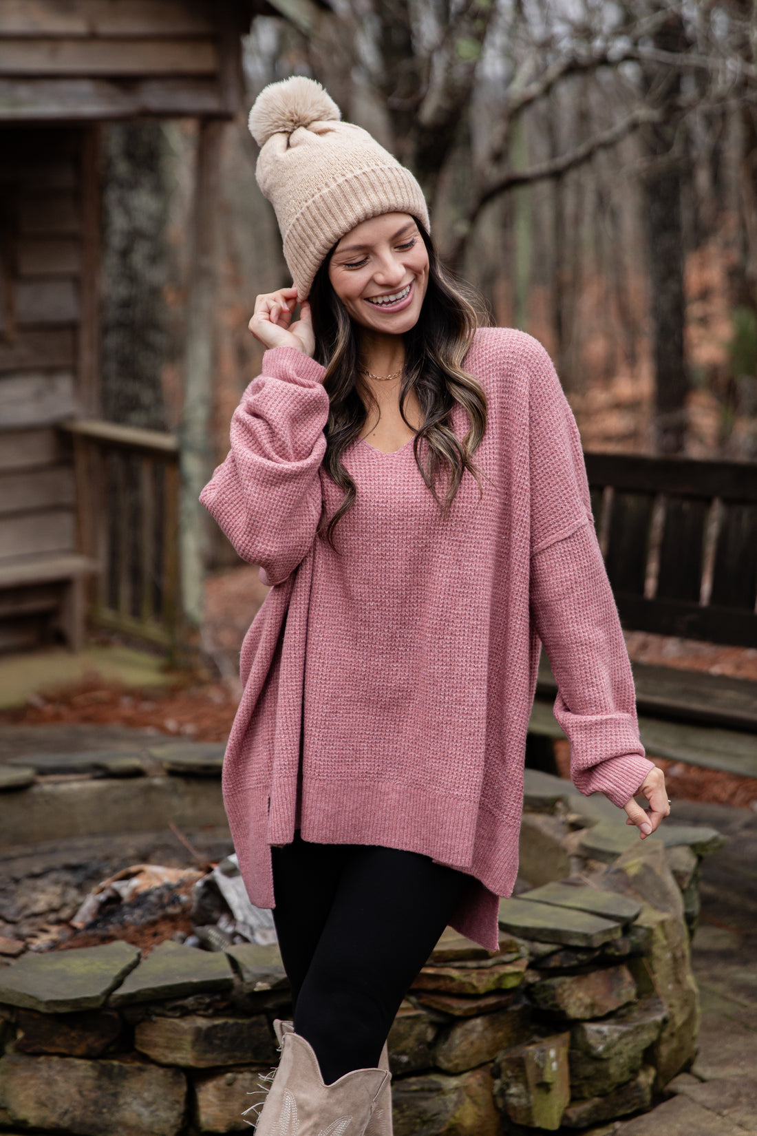Woman wearing a pink sweater and beanie standing near a fire pit.