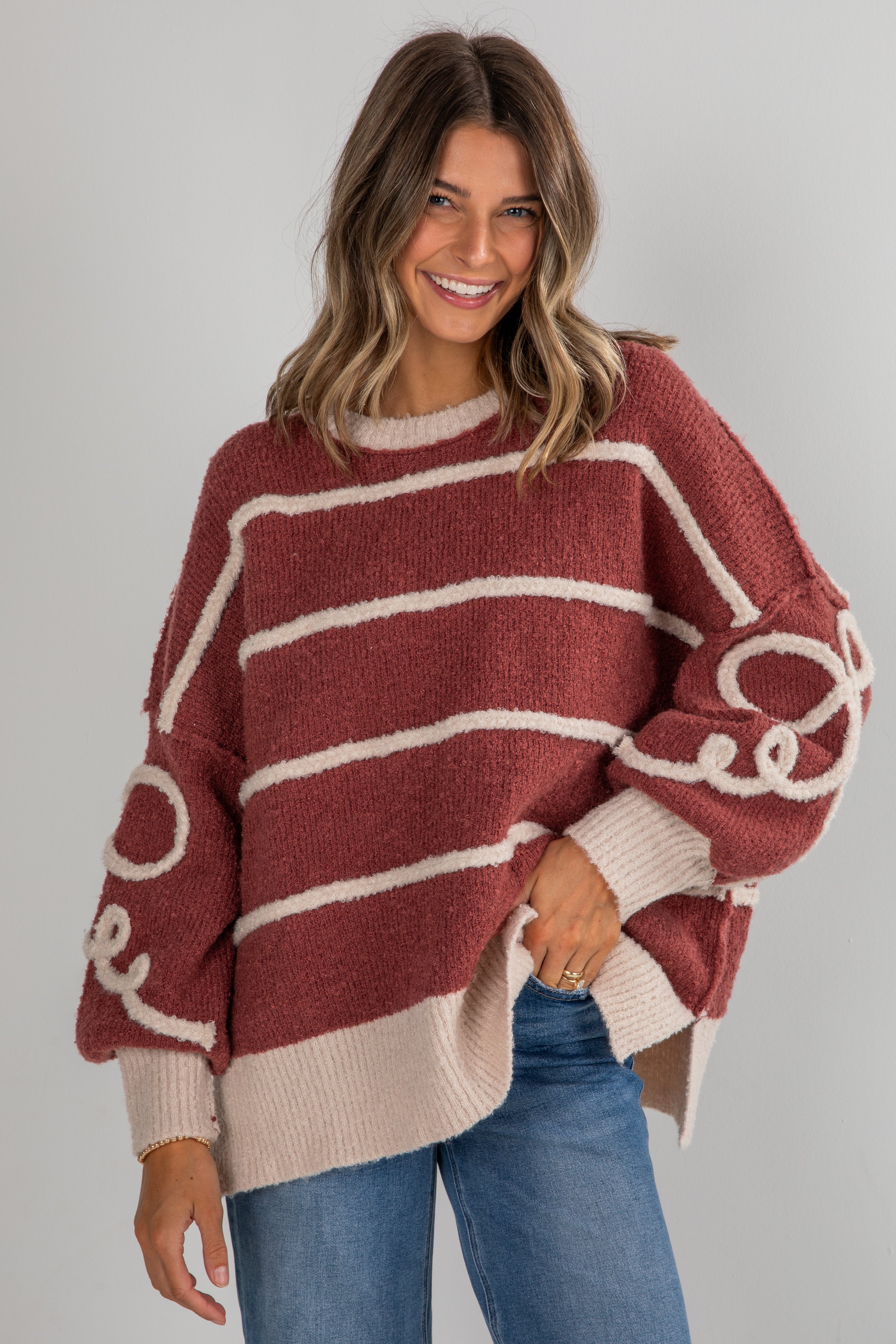 Woman wearing a maroon and beige striped sweater with a plain background