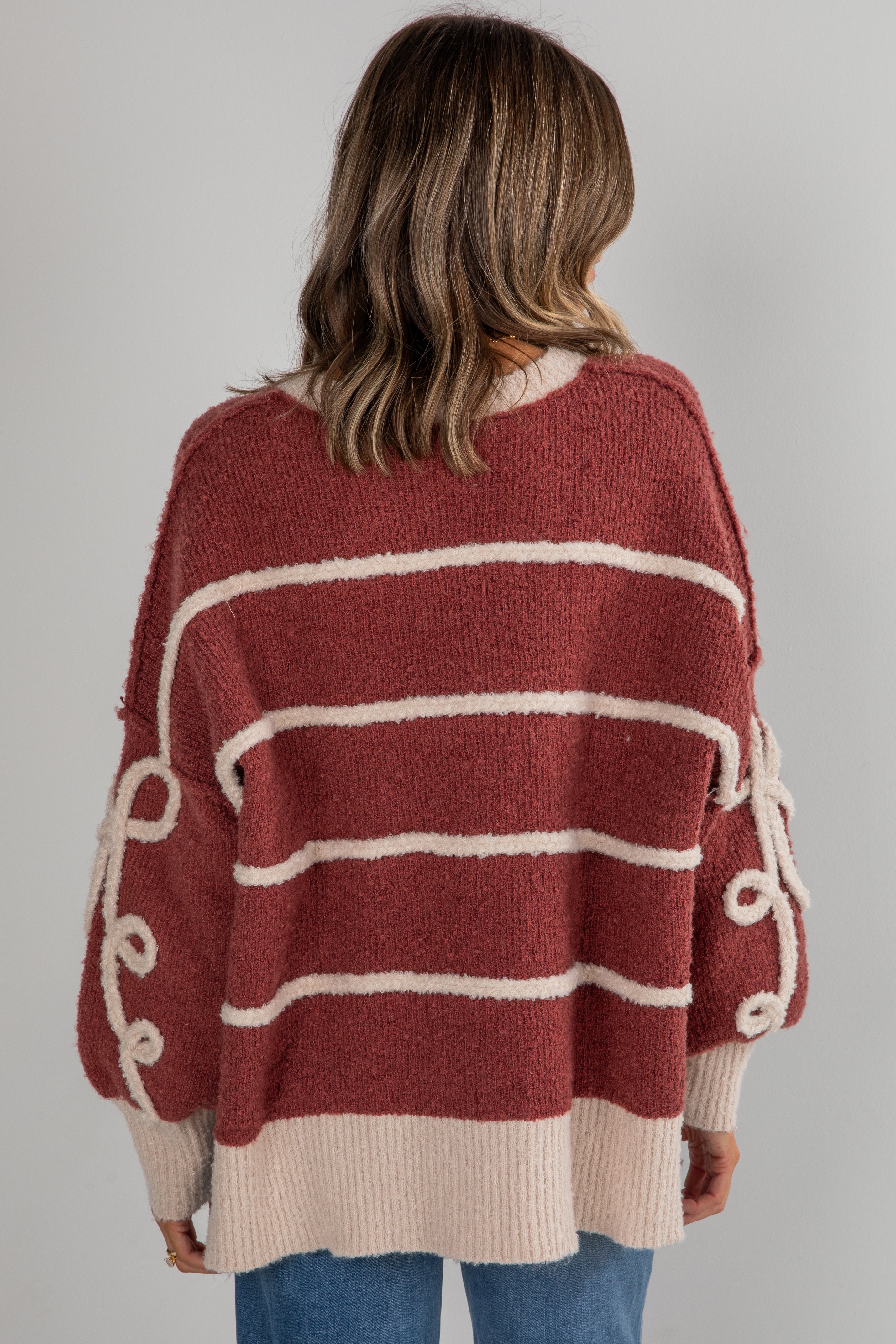 Person wearing a maroon and beige striped sweater on a plain background