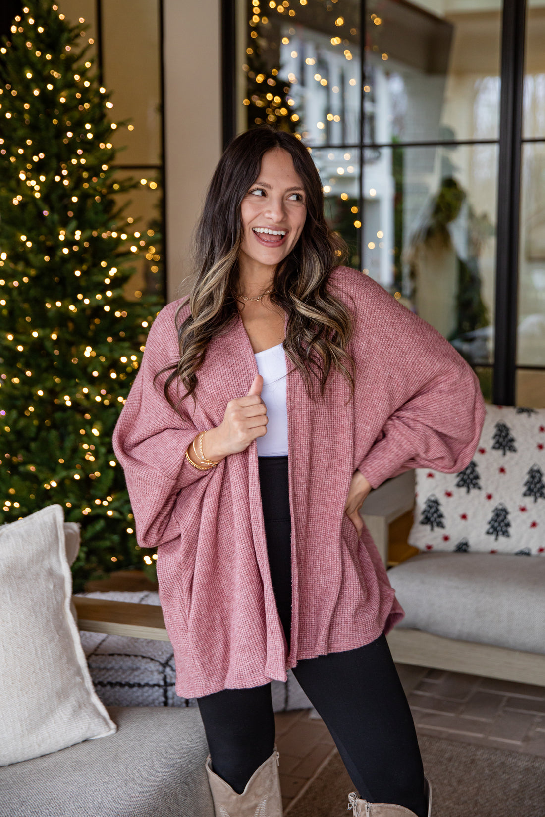 Woman wearing a pink cardigan in a cozy living room with Christmas decorations.