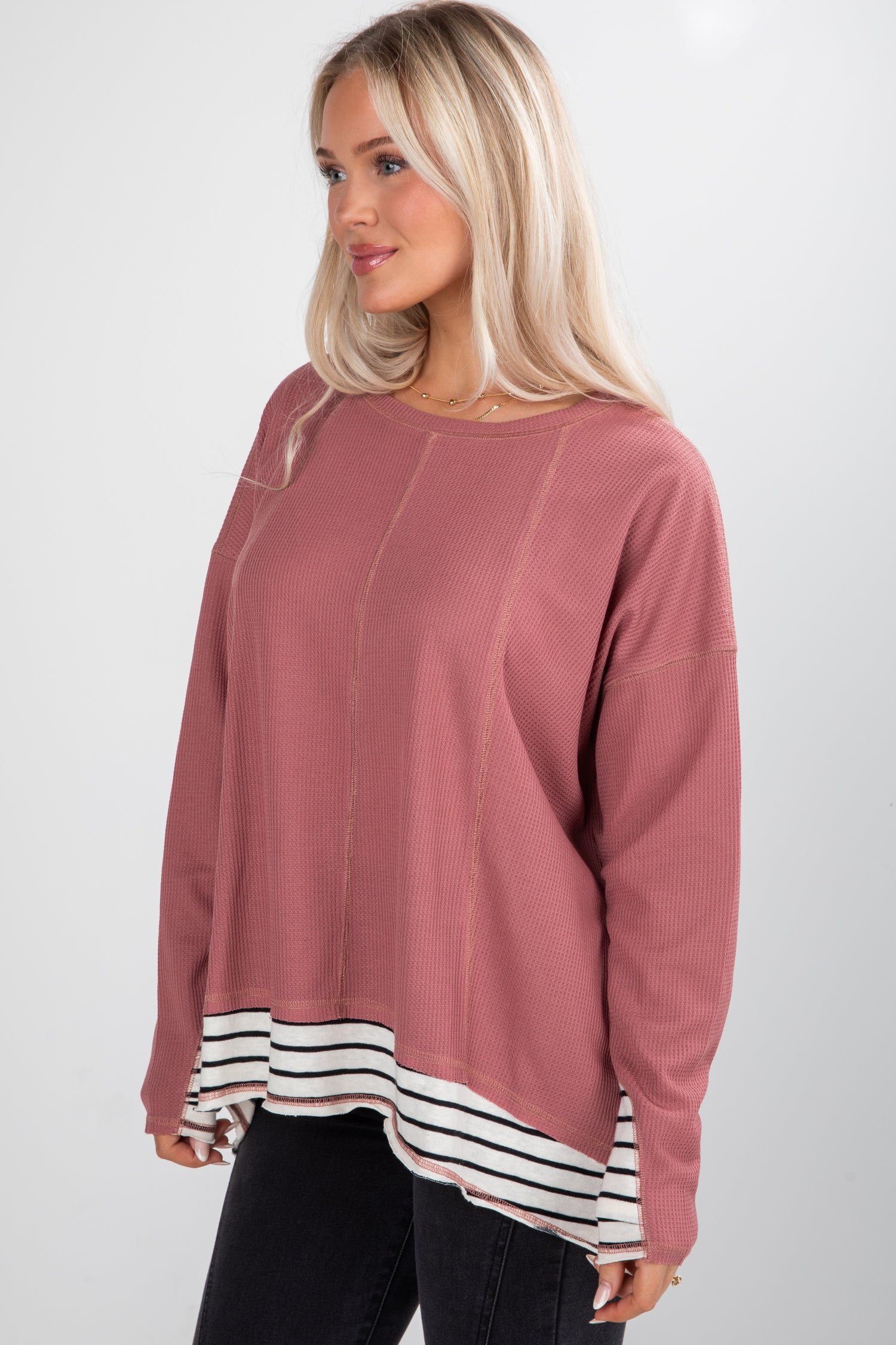 Woman wearing a pink sweater with a white and black striped hem on a white background