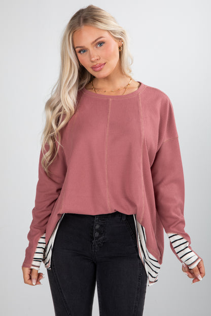 Woman wearing a pink sweater with black and white striped sleeves on a white background