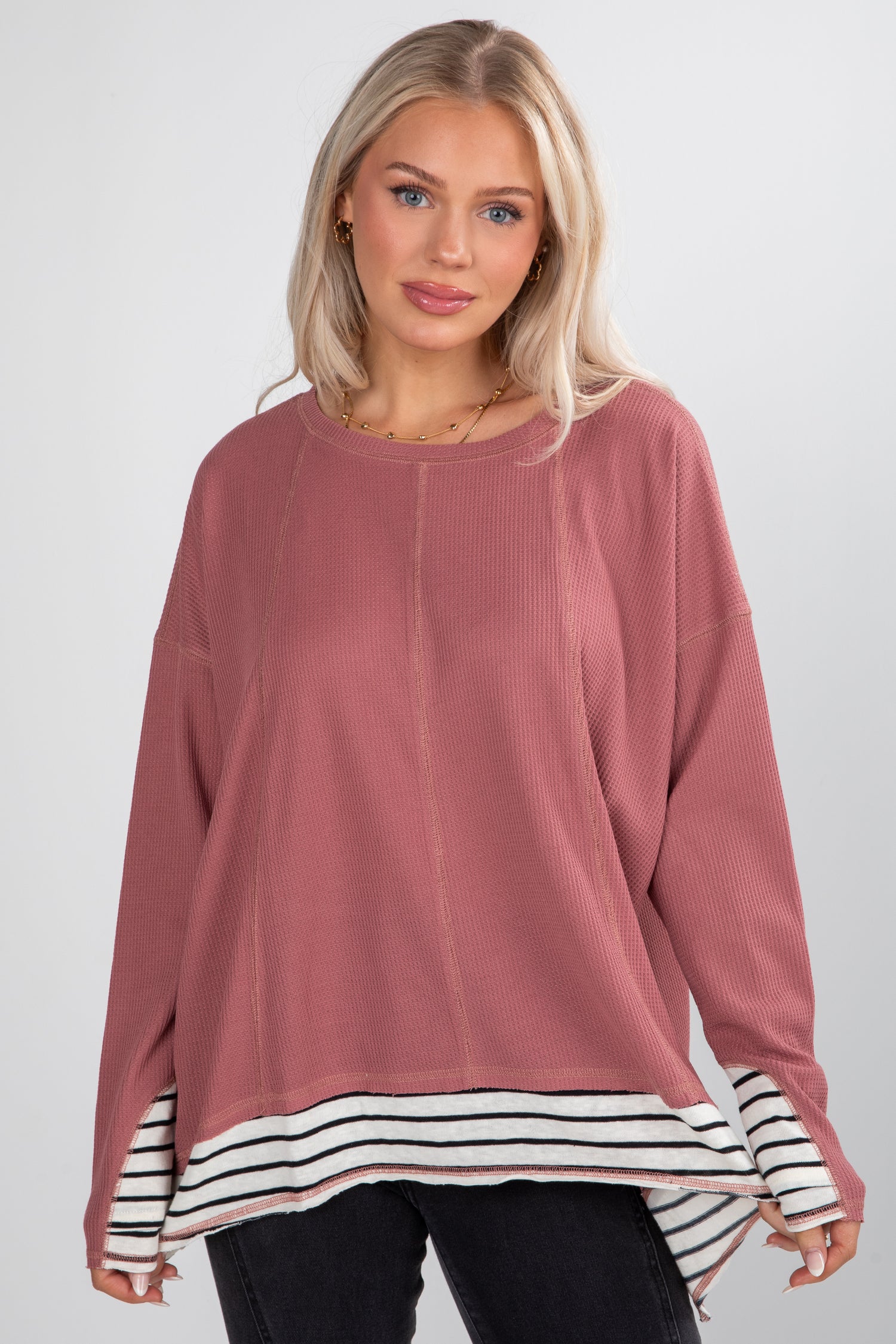 Woman wearing a pink long-sleeve top with a striped hem on a white background