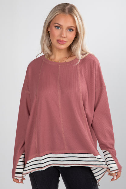 Woman wearing a pink long-sleeve top with a striped hem on a white background