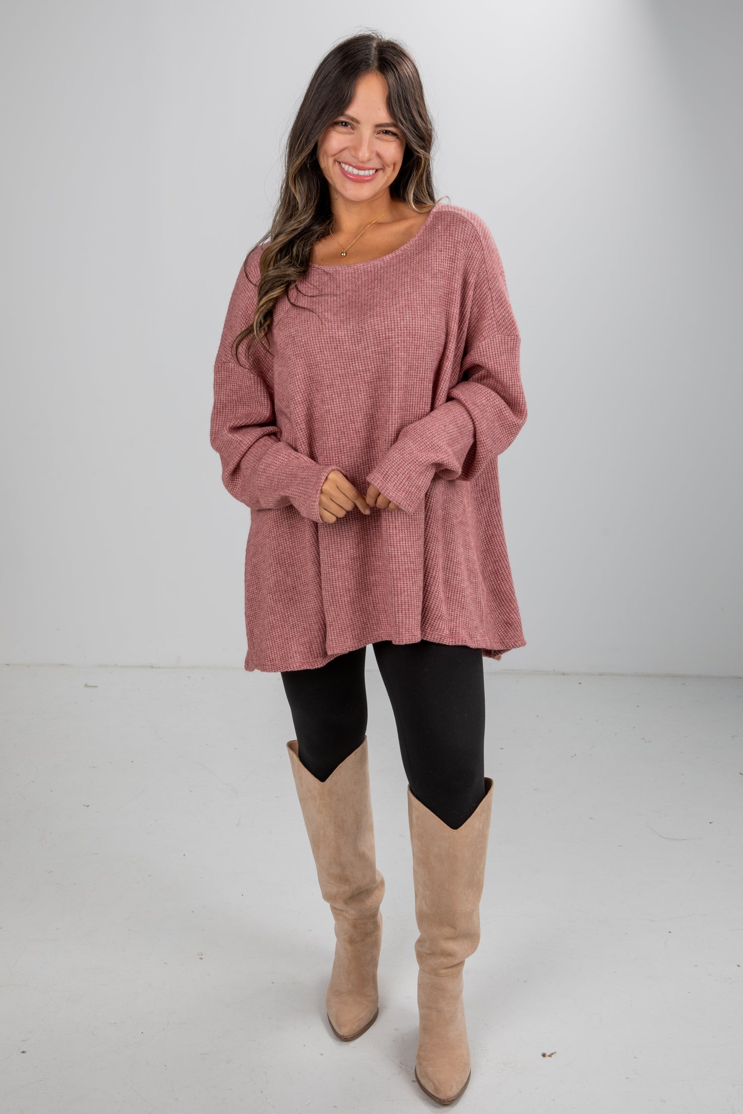 Woman wearing a pink sweater and beige knee-high boots on a white background