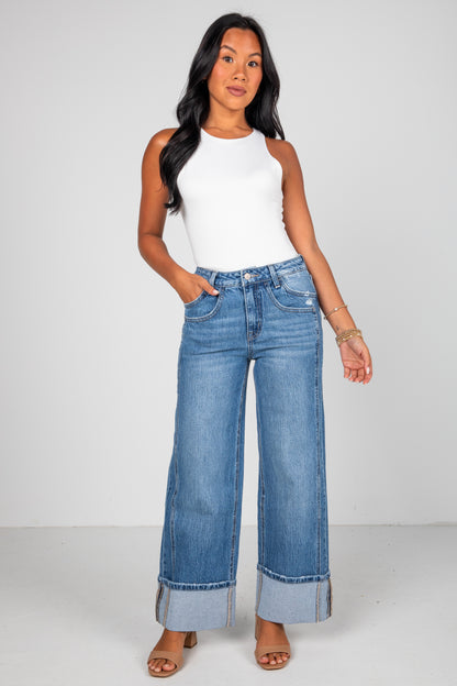 Woman wearing a white sleeveless top and blue jeans on a white background