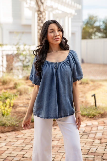 Woman wearing a blue top and white pants standing outdoors.