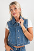 Woman wearing a denim vest over a white shirt on a plain background