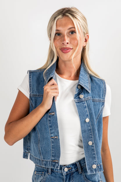 Woman wearing a denim vest over a white shirt on a plain background