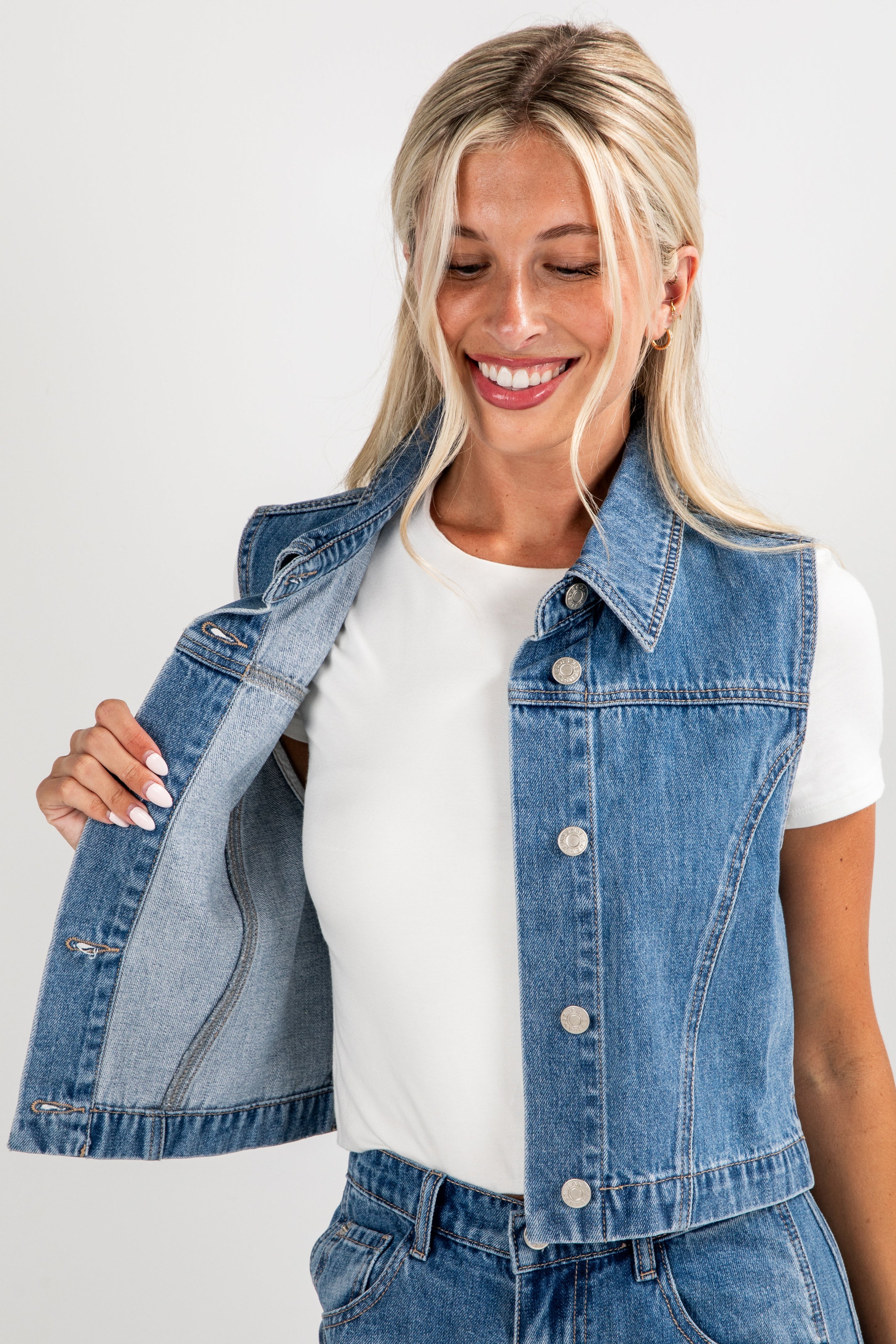 Woman wearing a denim vest over a white shirt on a plain background