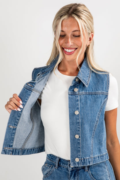 Woman wearing a denim vest over a white shirt on a plain background