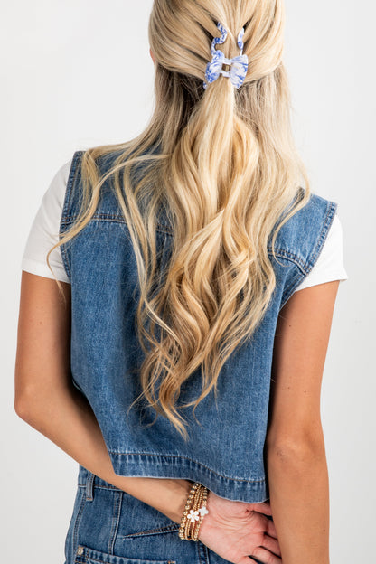 Person wearing a denim vest and white shirt with long blonde hair tied back, on a plain background
