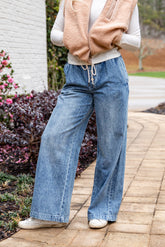 Person wearing a beige sweater, white shirt, blue jeans, and white sneakers on a paved walkway.