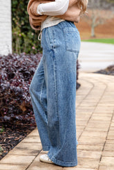 Person wearing blue jeans walking on a paved path with plants in the background