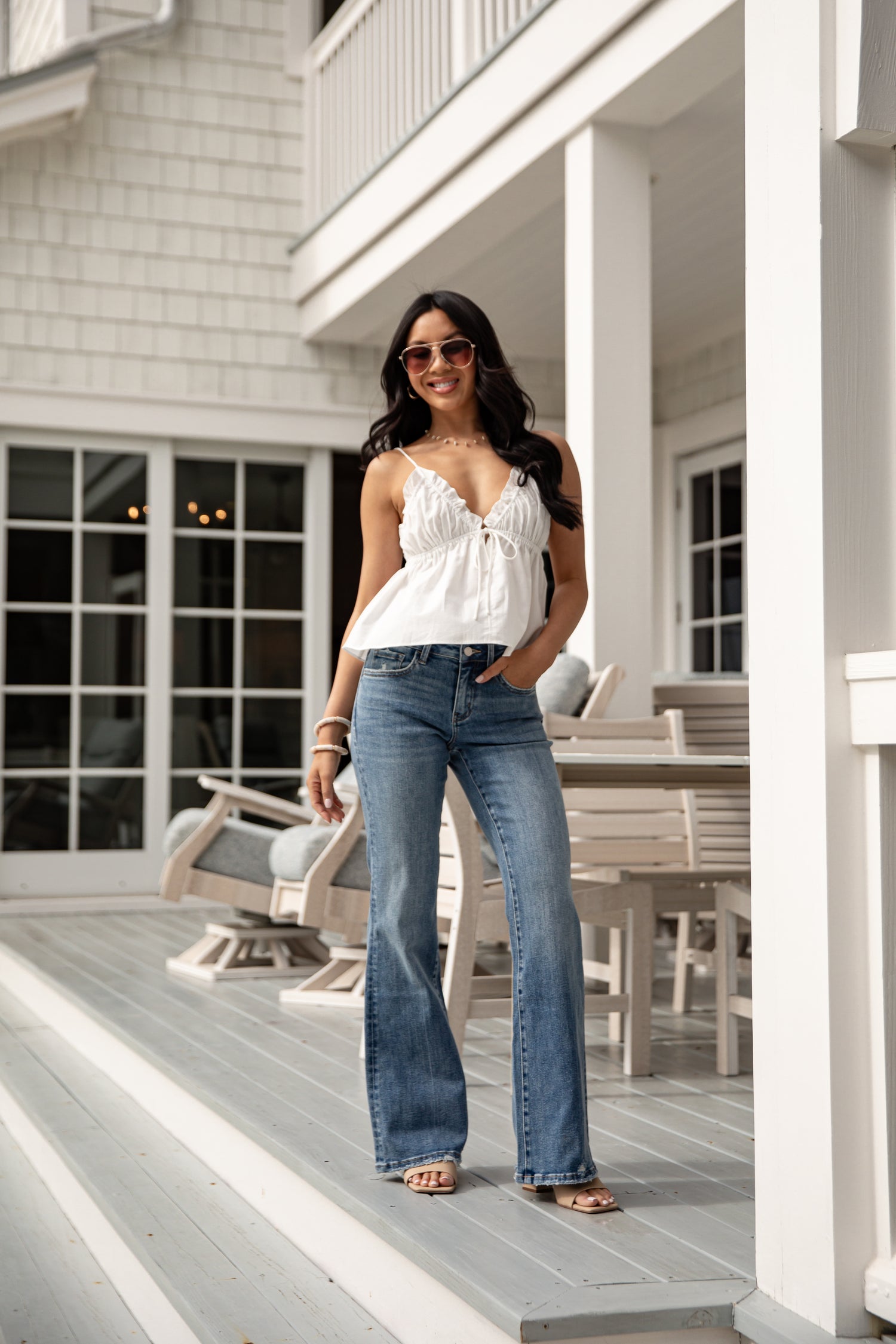Woman in a white top and blue jeans standing on a porch.