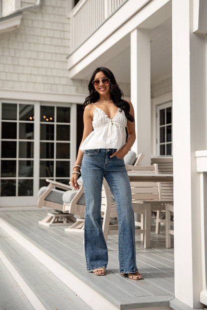 Woman in a white top and blue jeans standing on a porch.