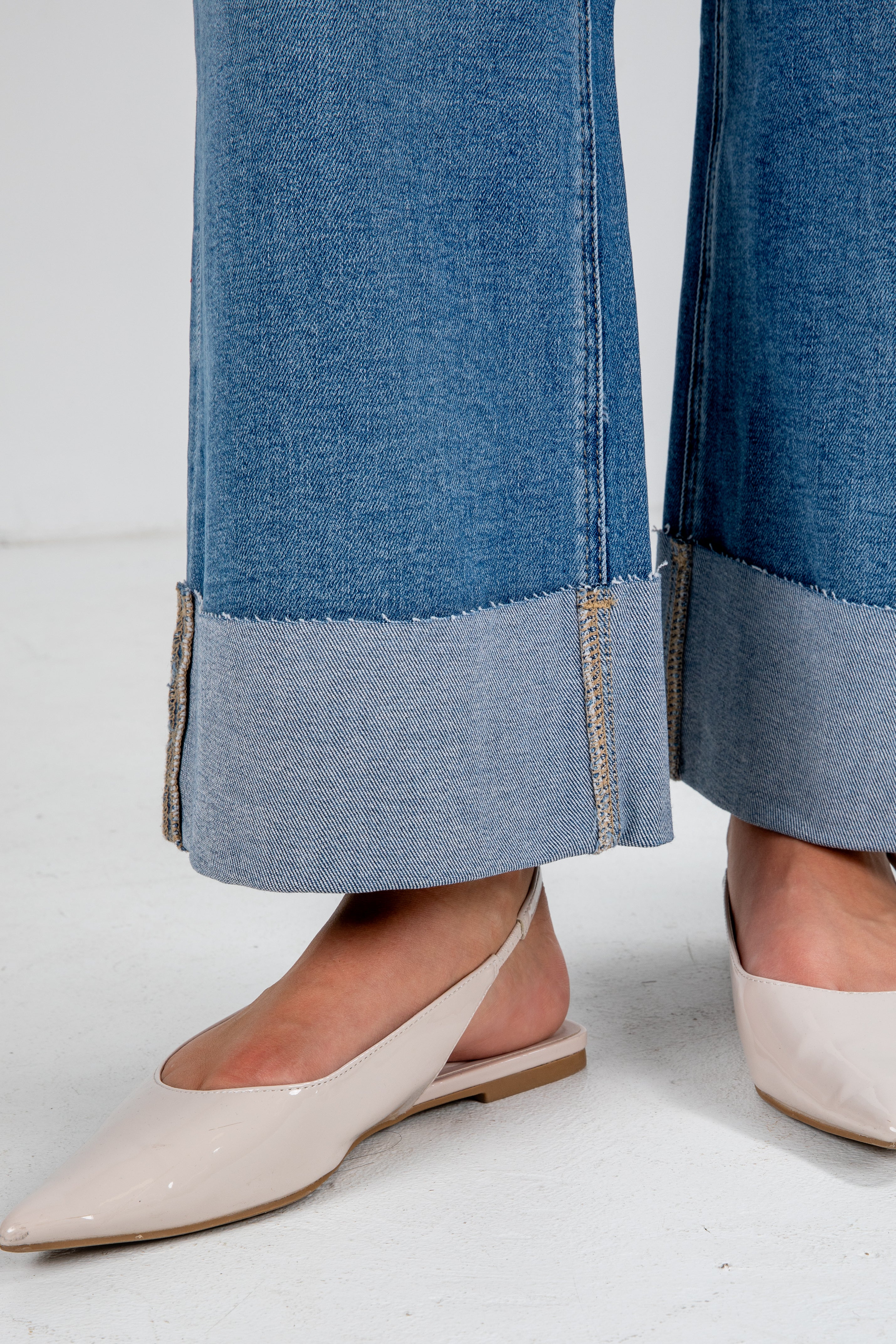 Close-up of blue jeans with a gray trim worn by a person wearing beige shoes on a white background