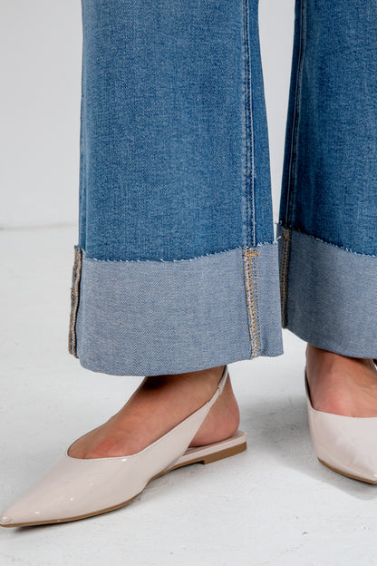 Close-up of blue jeans with a gray trim worn by a person wearing beige shoes on a white background