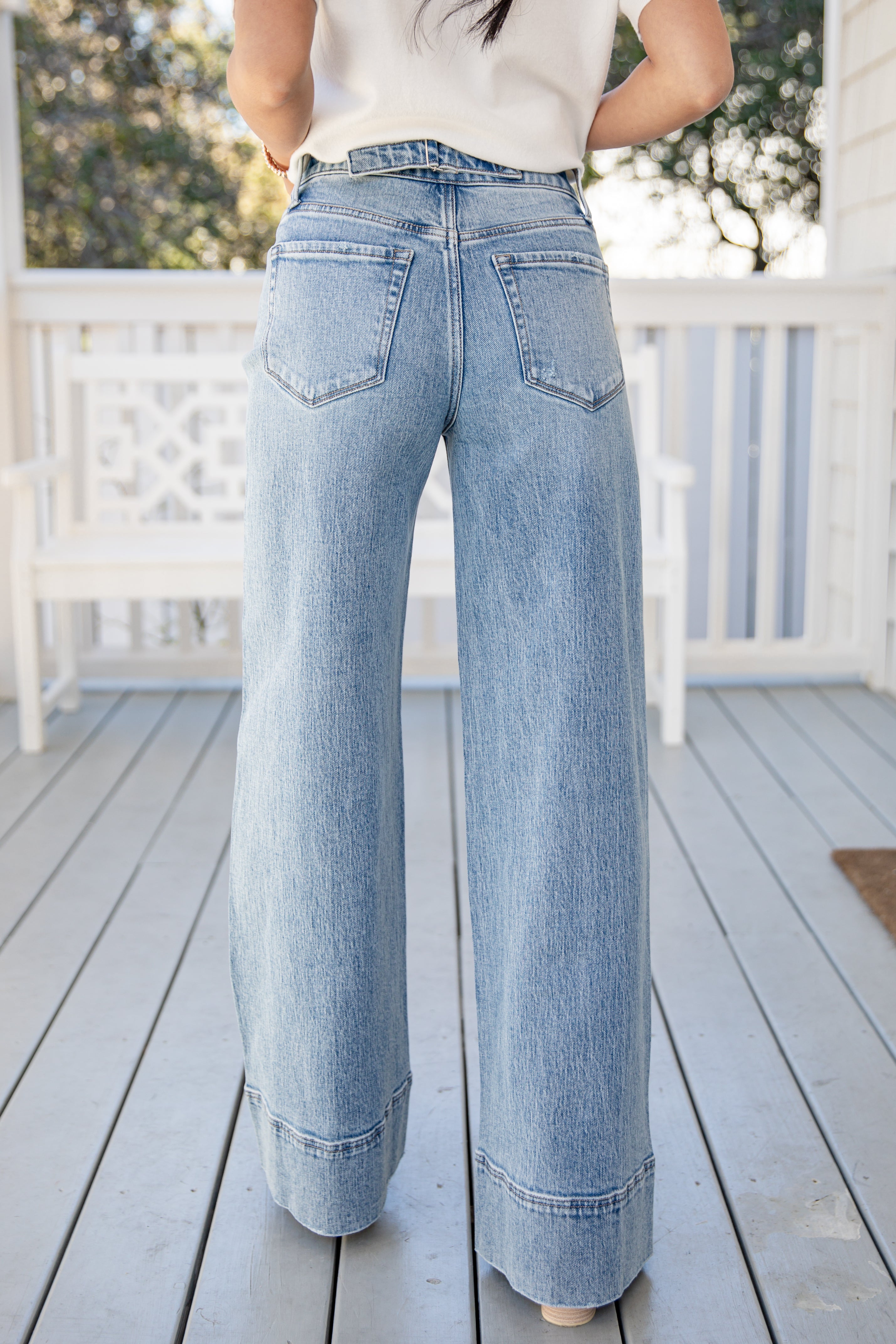 Person wearing light blue wide-leg jeans on a wooden deck.