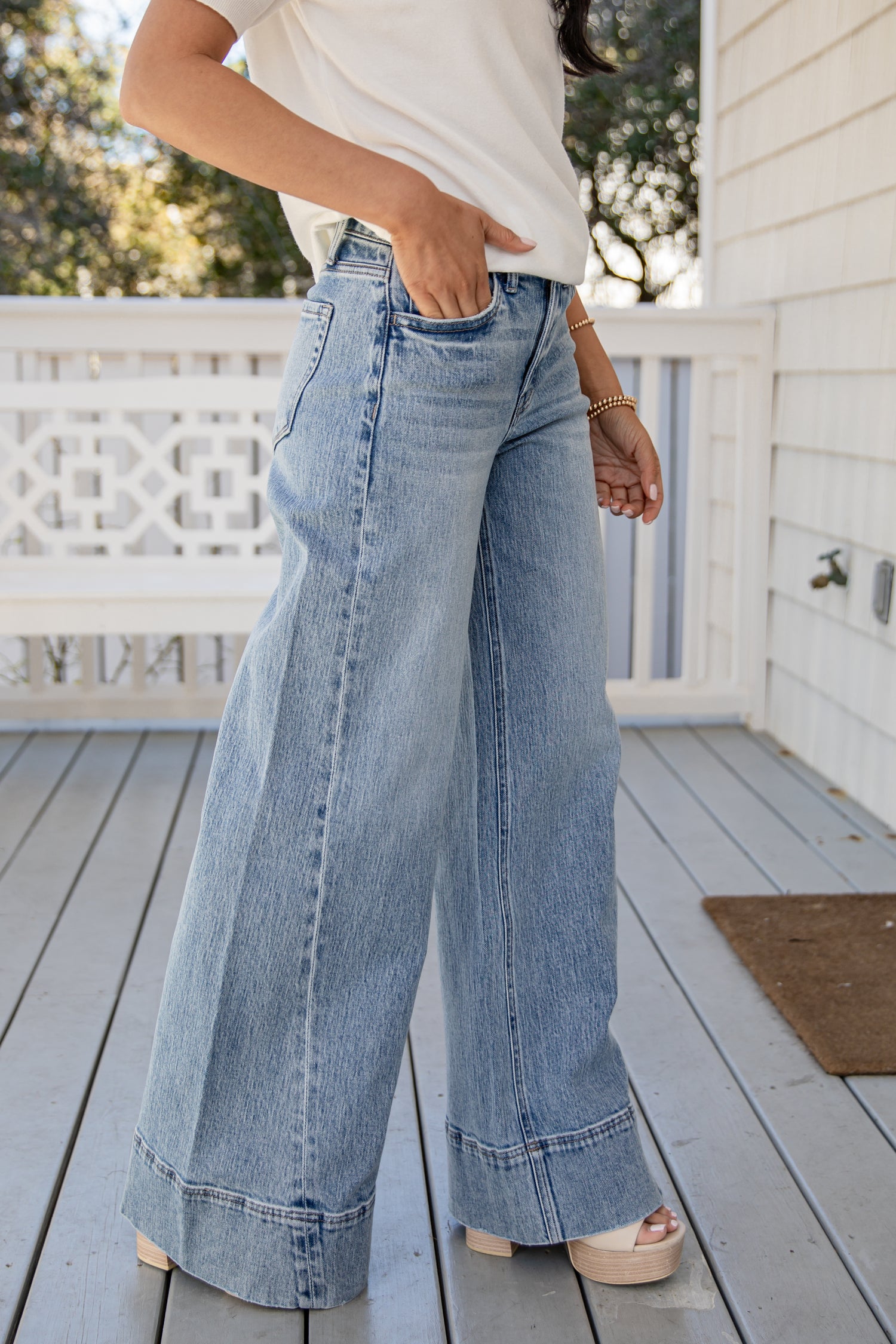 Person wearing light blue wide-leg jeans on a wooden deck.