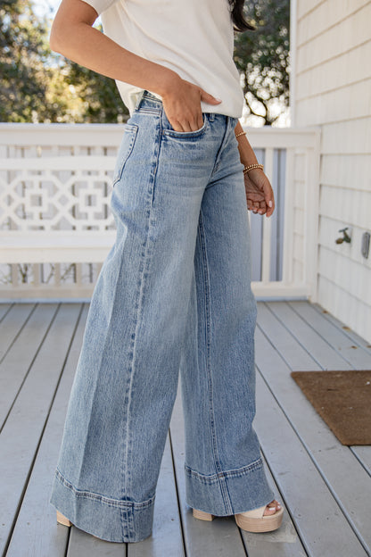 Person wearing light blue wide-leg jeans on a wooden deck.