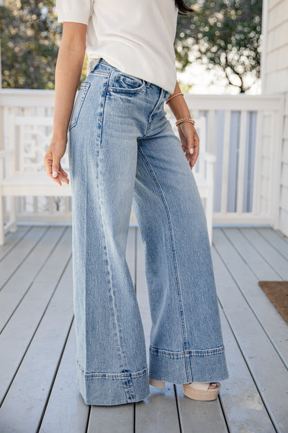 Person wearing light blue wide-leg jeans on a wooden deck.