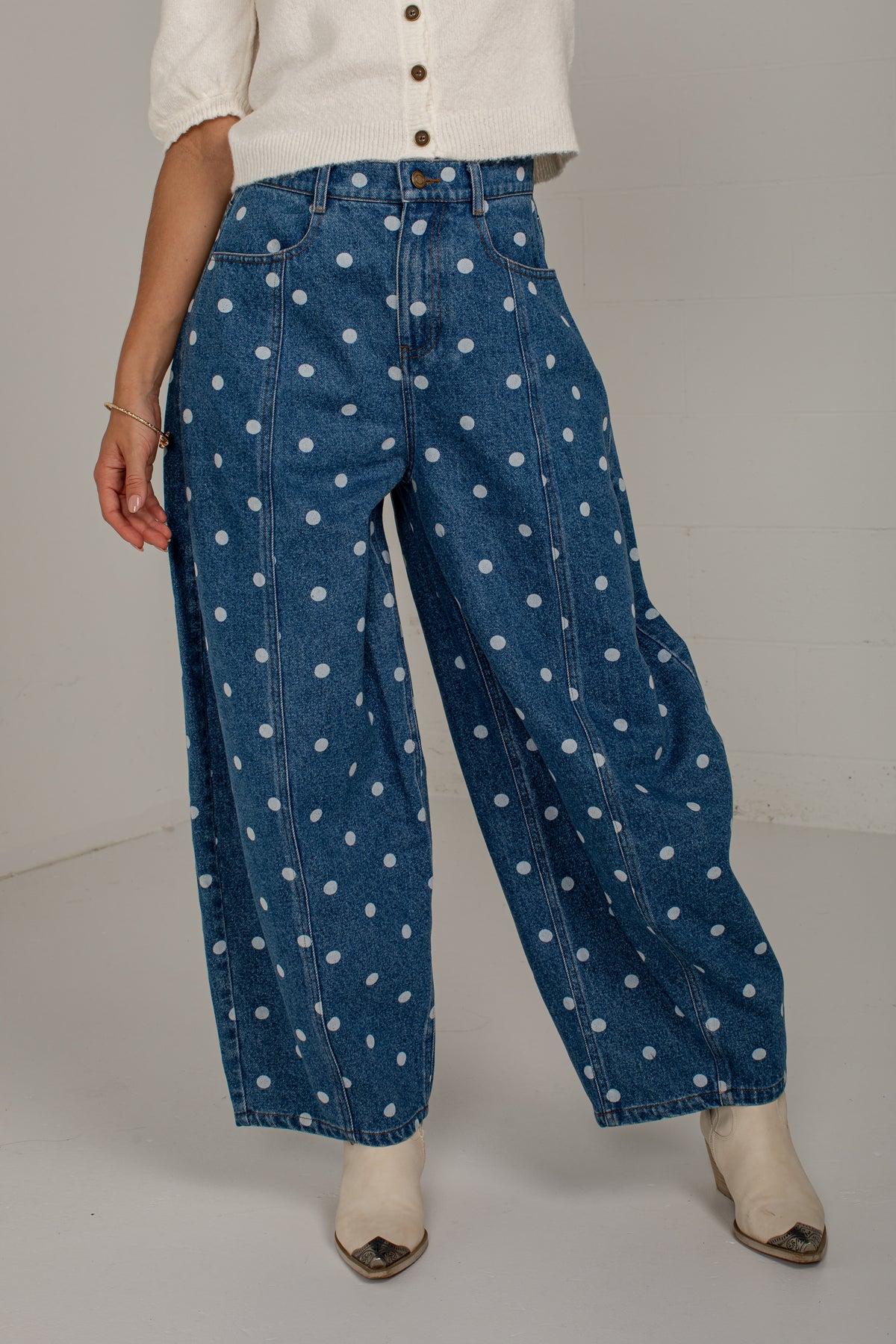 Angled front view of medium wash polka dot barrel jeans styled with an ivory knit cardigan and cream boots.