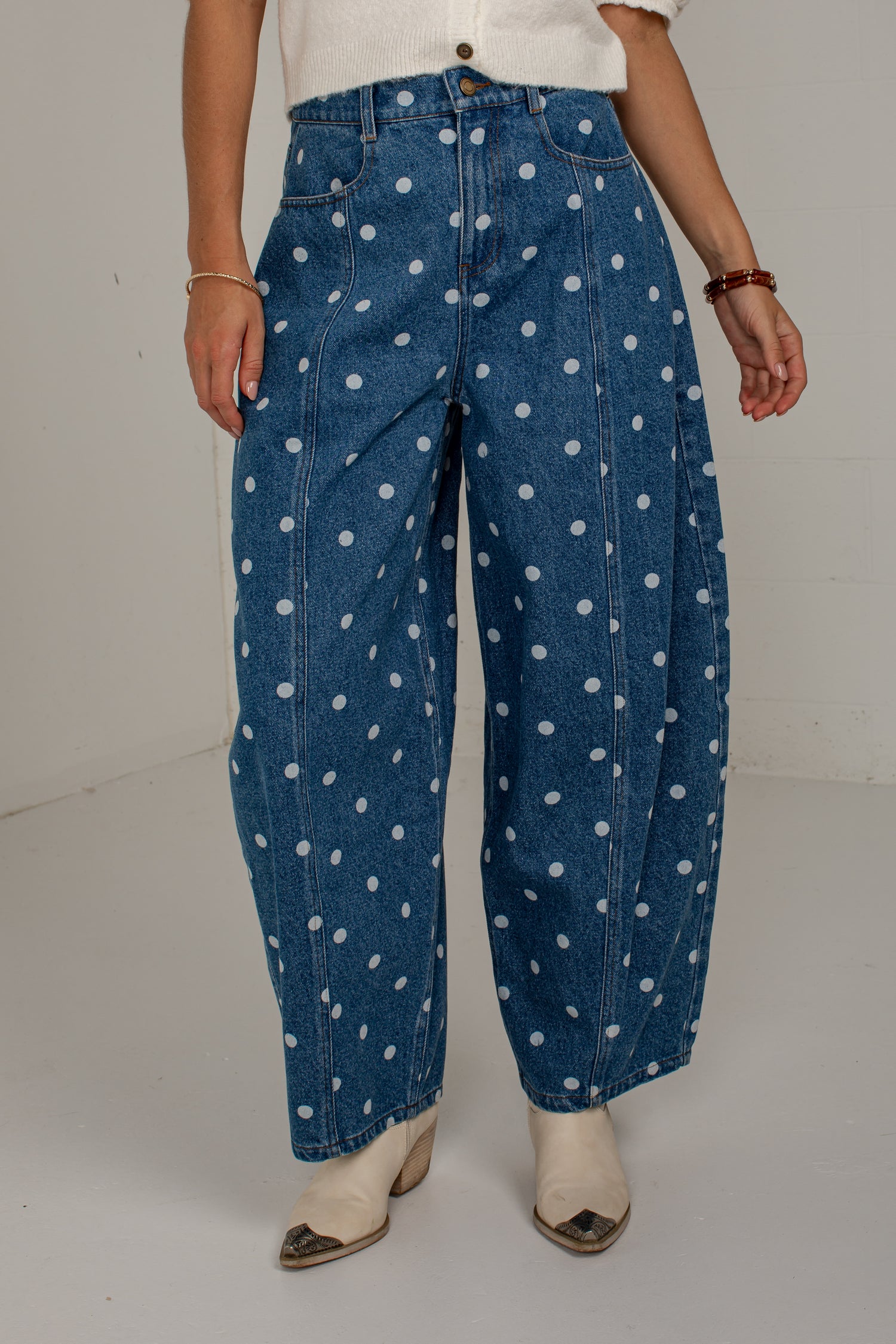 Front detail of medium wash polka dot jeans showing the high-rise fit, pockets, and barrel-leg silhouette.