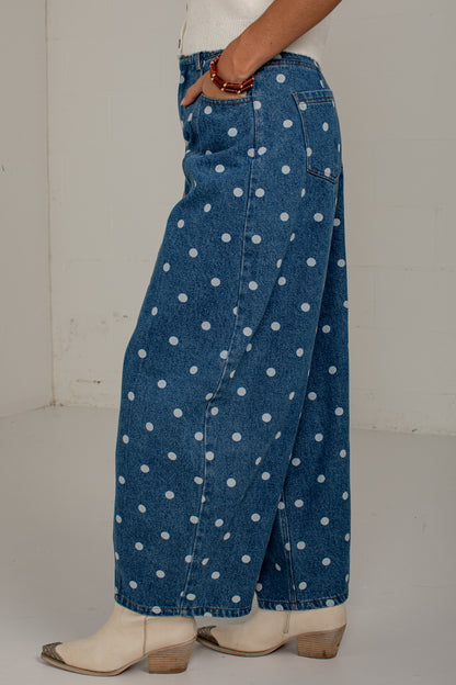 Model lifting one leg to show the relaxed fit and curved silhouette of medium wash polka dot barrel jeans.