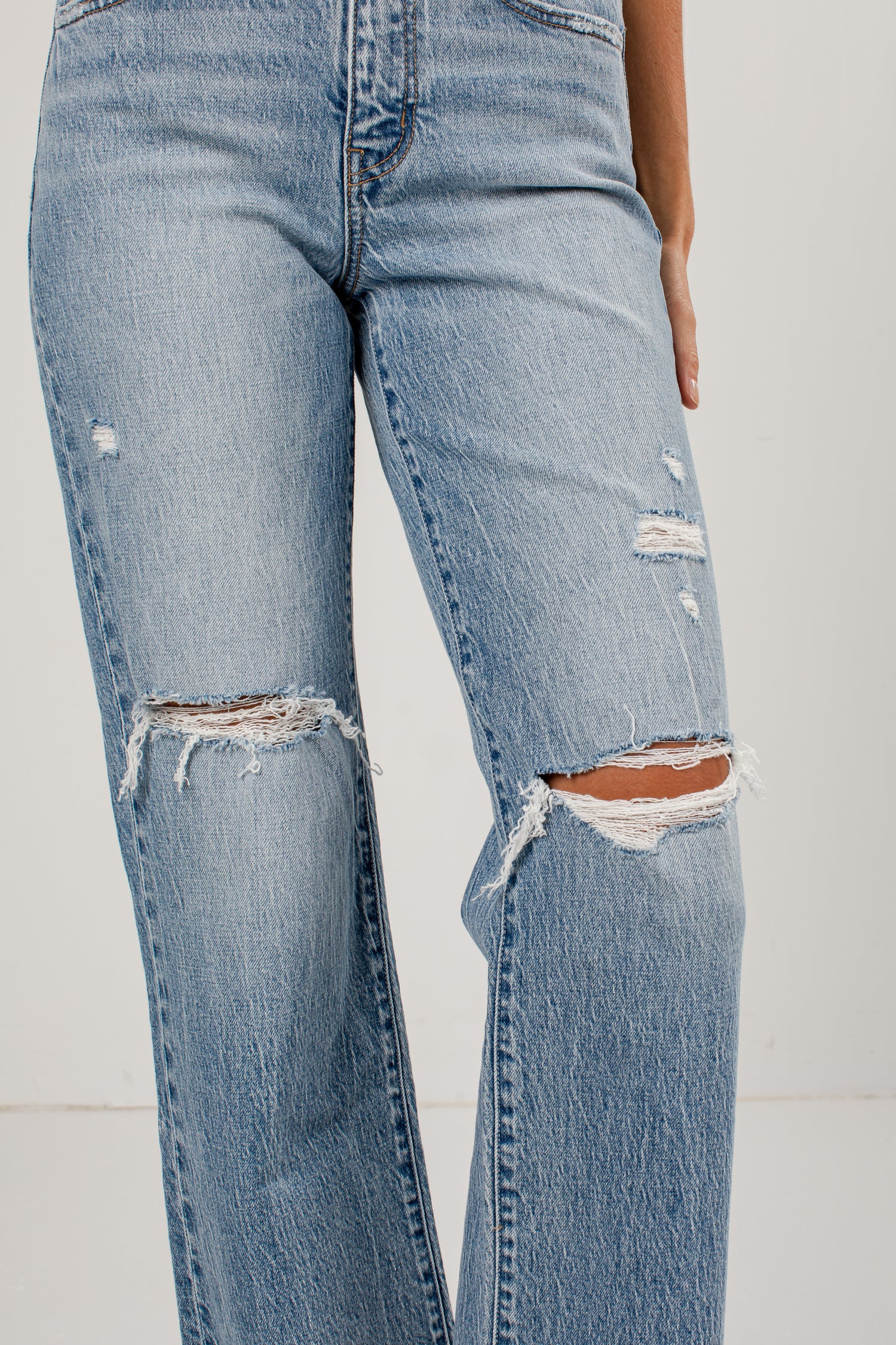 Light wash blue distressed jeans with ripped details on the thighs and knees, shown on a model against a plain light background.