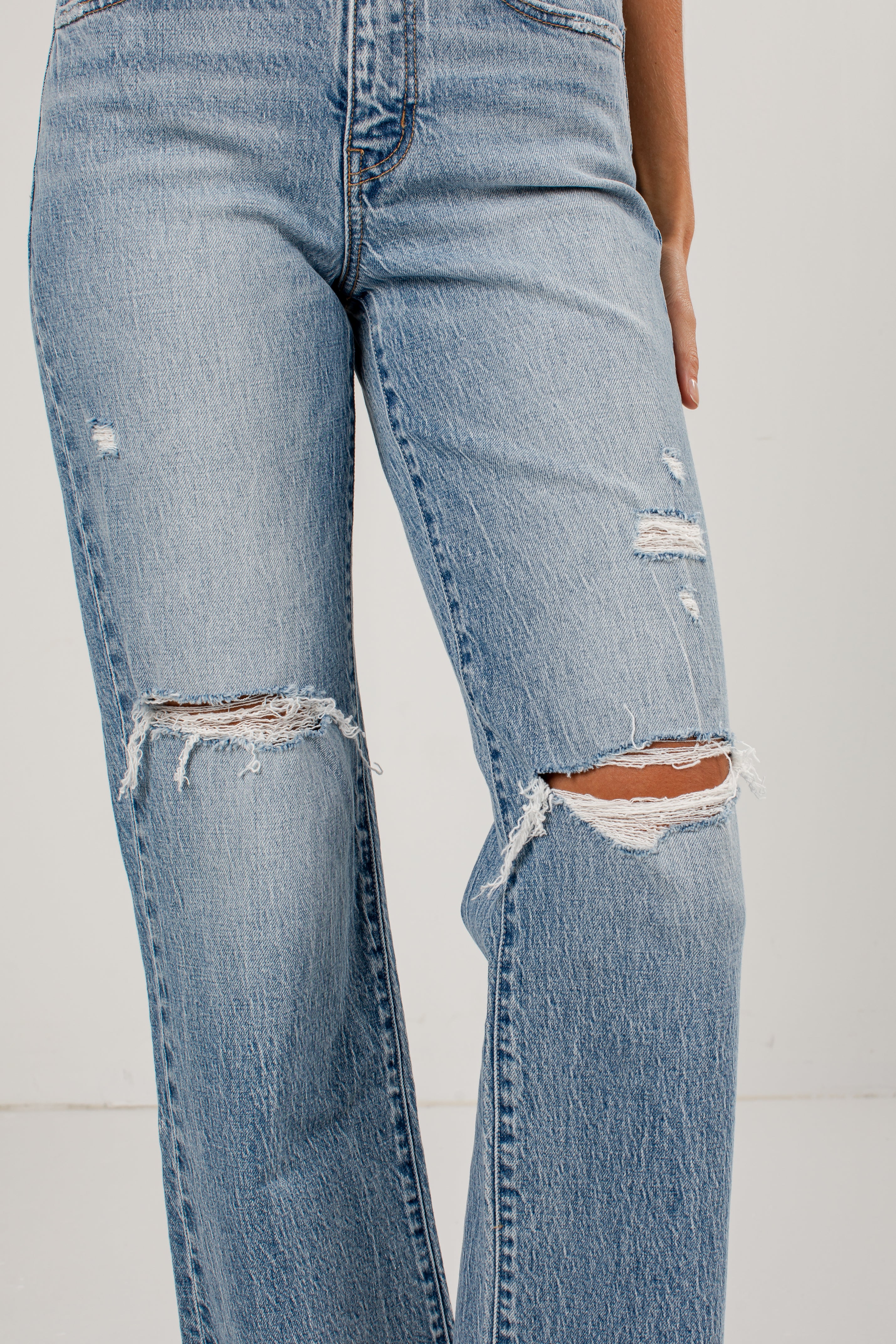 Light wash blue distressed jeans with ripped details on the thighs and knees, shown on a model against a plain light background.