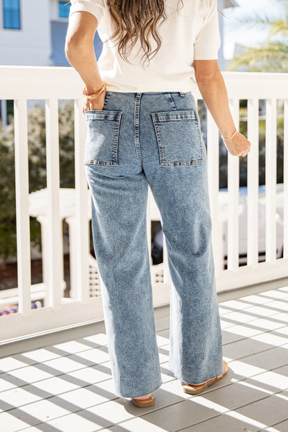 Person wearing light blue jeans and a white top on a balcony.
