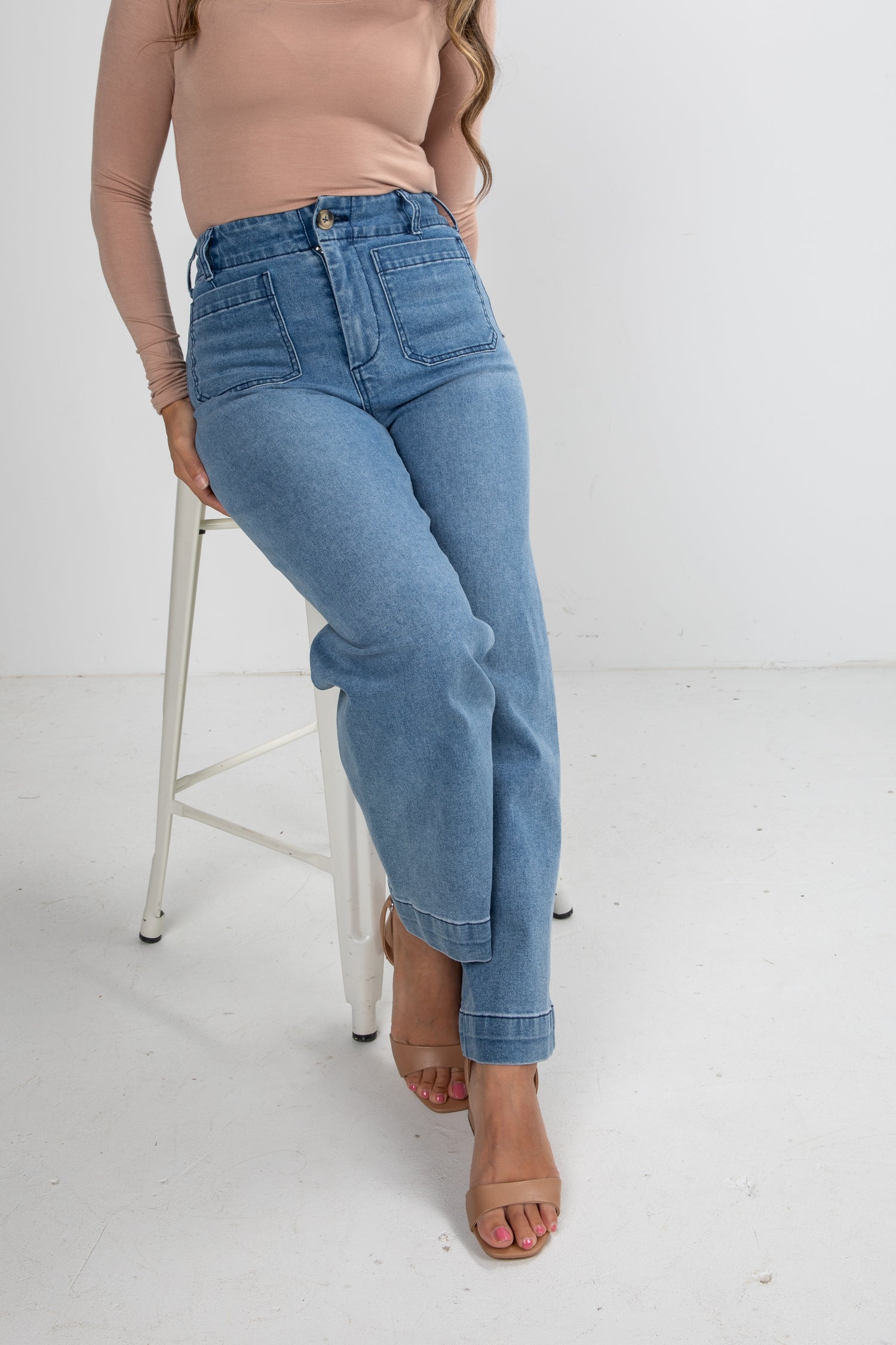 Person wearing light blue jeans sitting on a white stool against a white background
