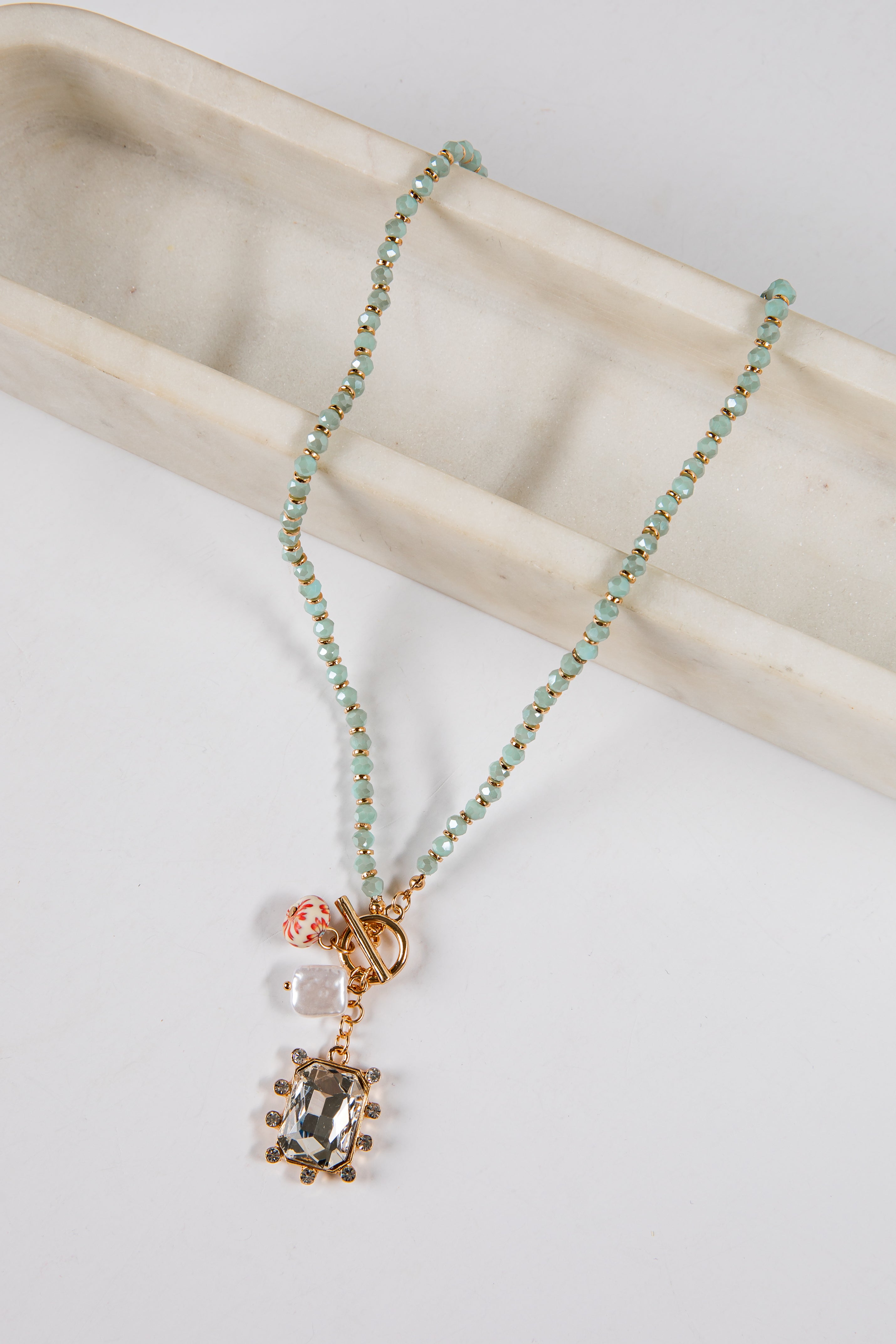 Necklace with green beads and a pendant on a light surface