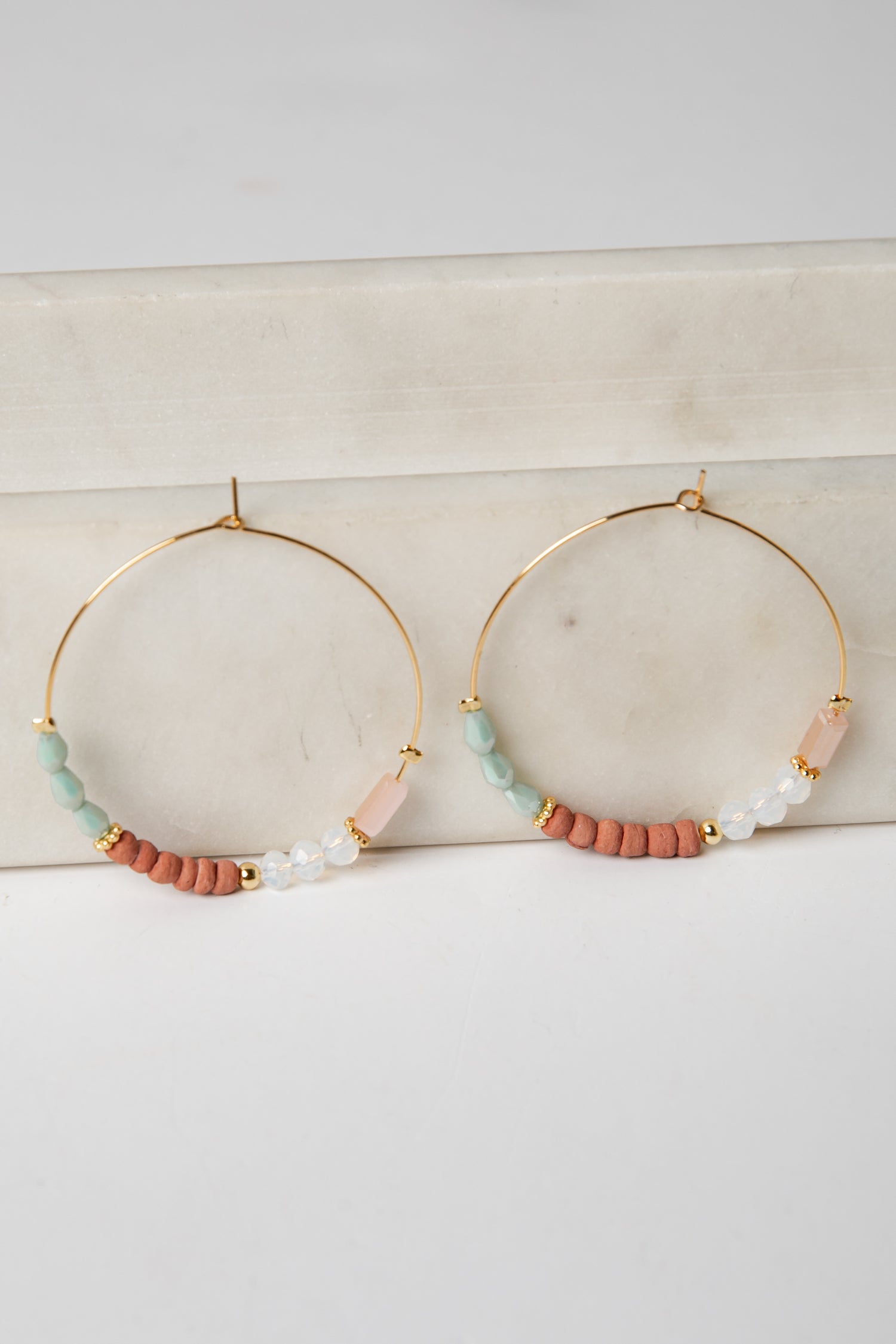 Gold hoop earrings with colorful beads on a light surface