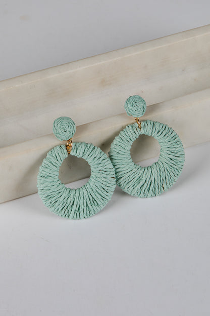 Pair of light blue circular earrings on a beige surface with a white background