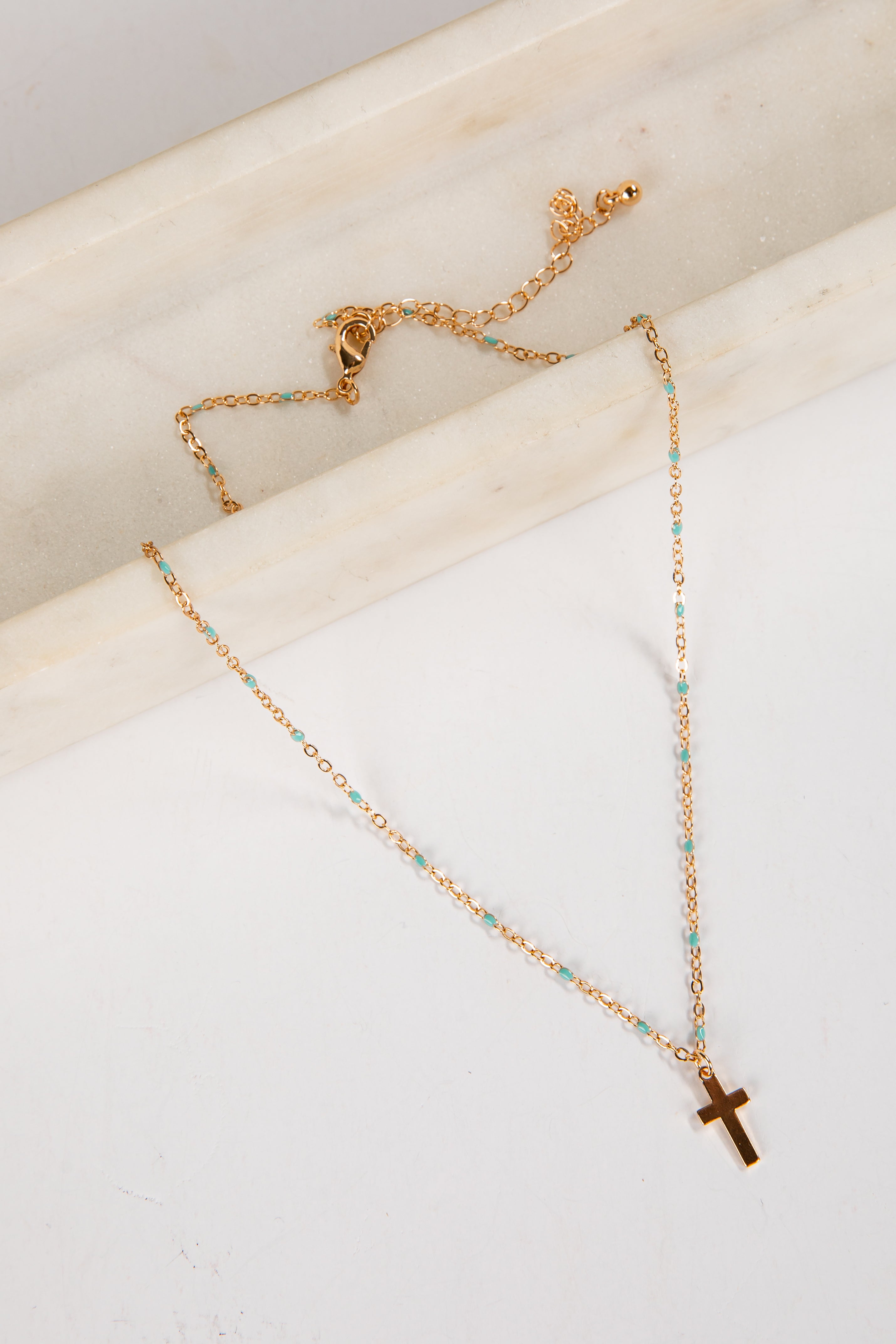 Gold necklace with a cross pendant on a marble surface