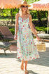 Woman in a floral dress standing under peach-colored umbrellas in a sunlit outdoor setting.