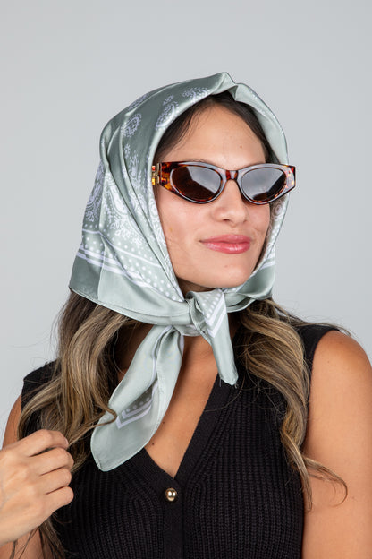 Woman wearing a light gray headscarf and sunglasses on a plain background