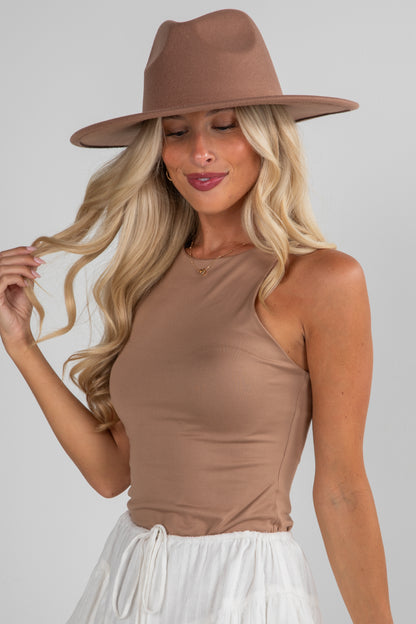 Woman wearing a brown hat and sleeveless top with a white skirt on a light gray background