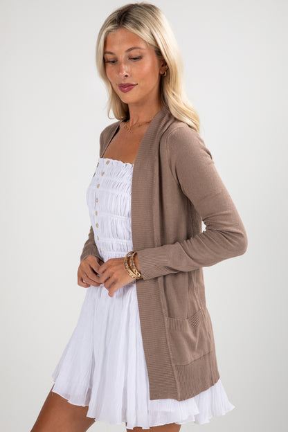 Woman wearing a brown cardigan over a white dress on a plain background