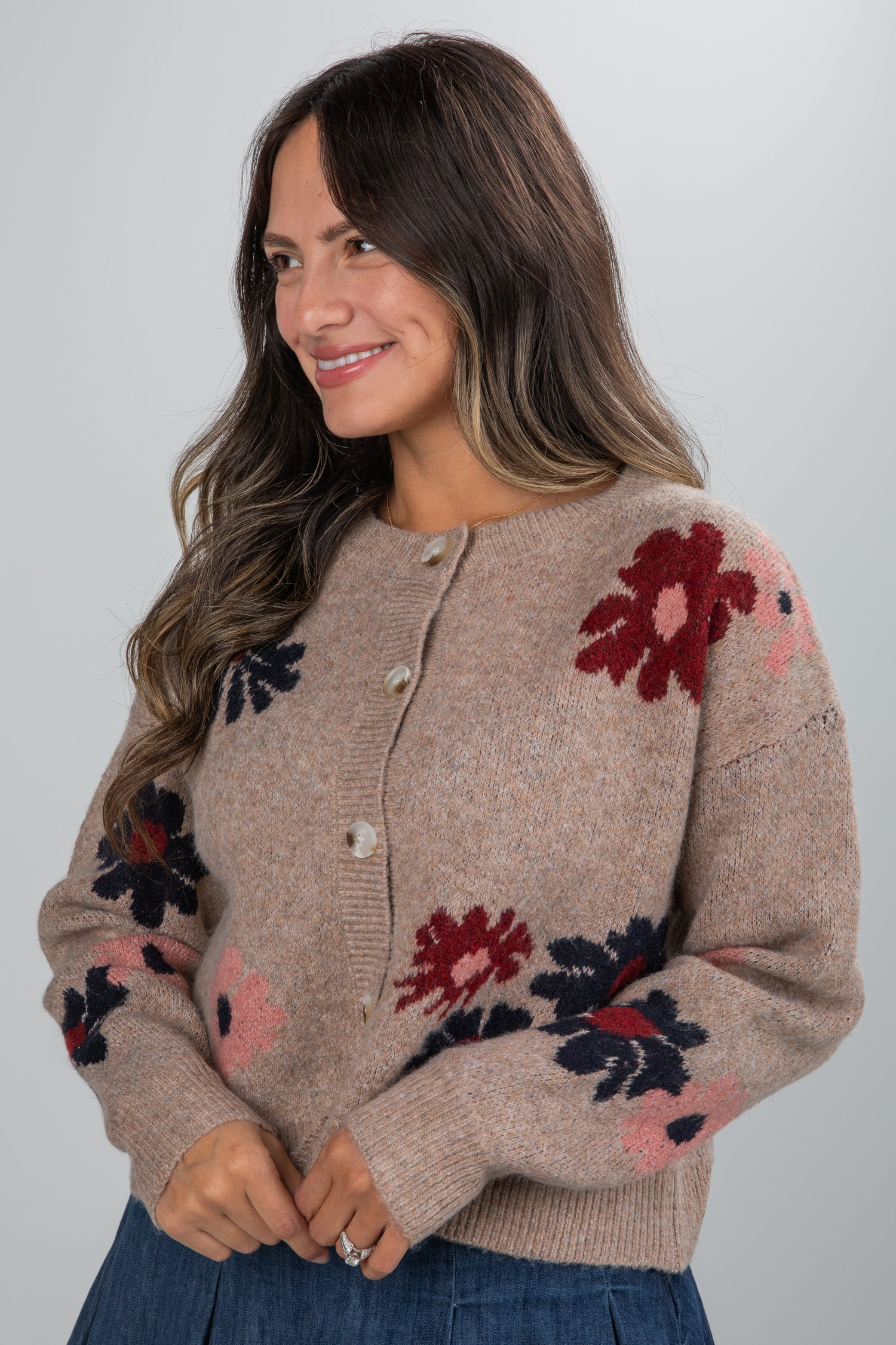 Woman wearing a beige cardigan with floral patterns on a plain background