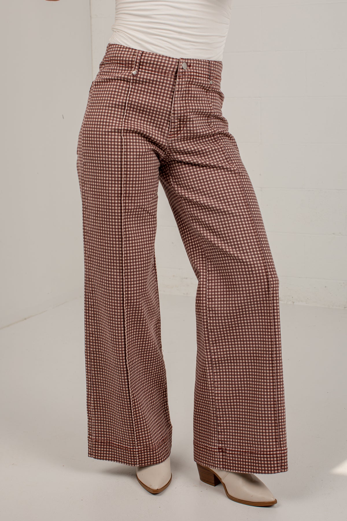 A person wearing high-waisted, wide-leg trousers with a brown and white houndstooth pattern, styled with a white top and white heeled mules.