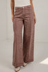 A model wearing high-waisted, wide-leg trousers with a brown and beige houndstooth pattern, paired with a white top and beige boots.